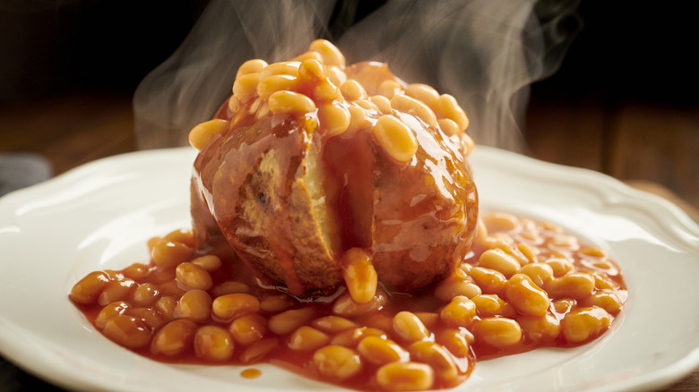 Steaming baked potato on white plate, topped with baked beans