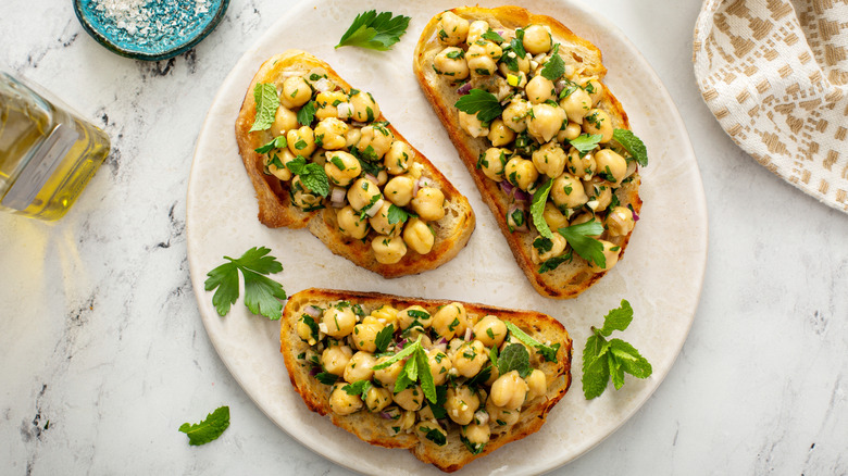 Three slices on toast on plate, topped with chickpeas, herbs, and red onion