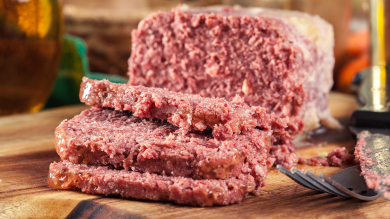 Sliced canned corned beef on wooden cutting board