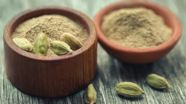 Ground cardamom and whole cardamom pods in wooden bowls
