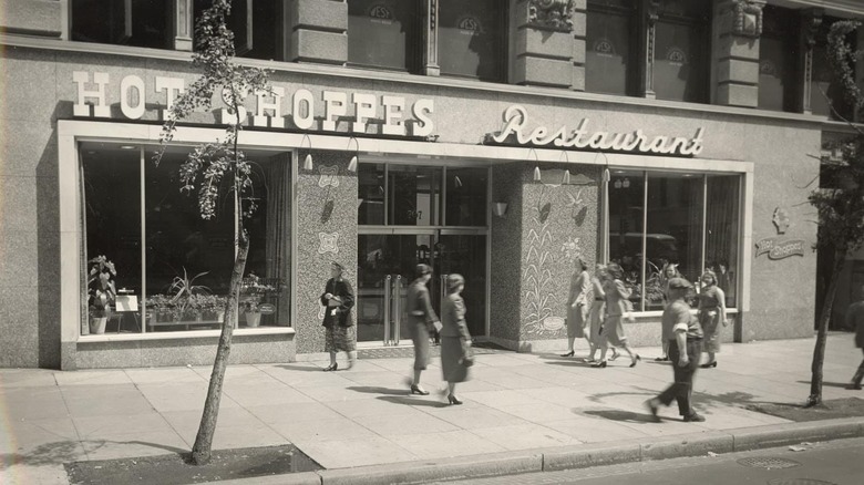 Black and white image of people walking on sidewalk outside Hot Shoppes restaurant