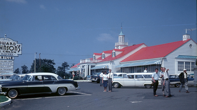Old photo of people walking in a Howard Johnson's parking lot with restaurant behind