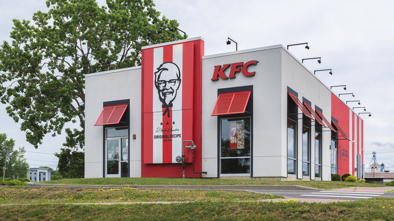 The exterior of a KFC from the side entrance, surrounded by lawn with a large tree to the left