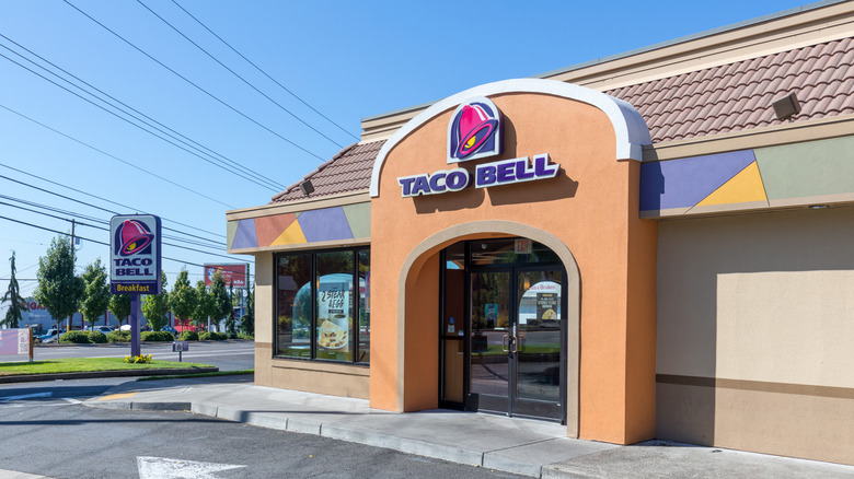 The front exterior of a Taco Bell with the street sign to the left