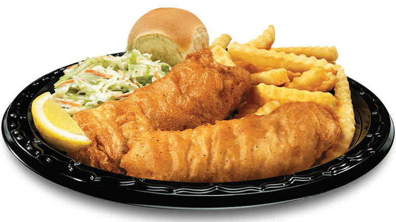 Fish and chips with coleslaw, dinner roll, and lemon wedge on black plastic plate
