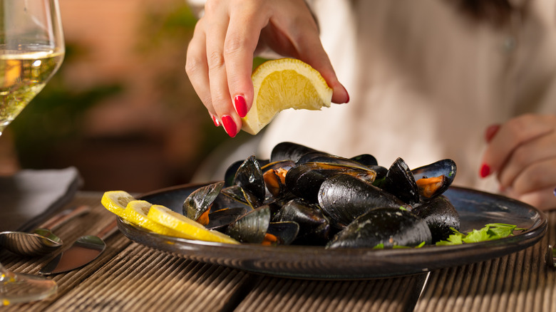 Hand squeezing lemon wedge over plate of mussels