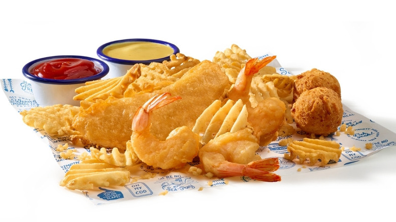 Fried fish, shrimp, waffle fries, and hushpuppies on parchment paper with two pots of dip