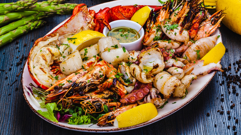 Platter of grilled seafood with lemon wedges and pot of herb butter sauce
