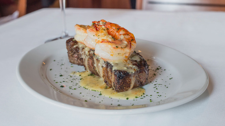Plate of steak topped with lobster tail and buttery sauce