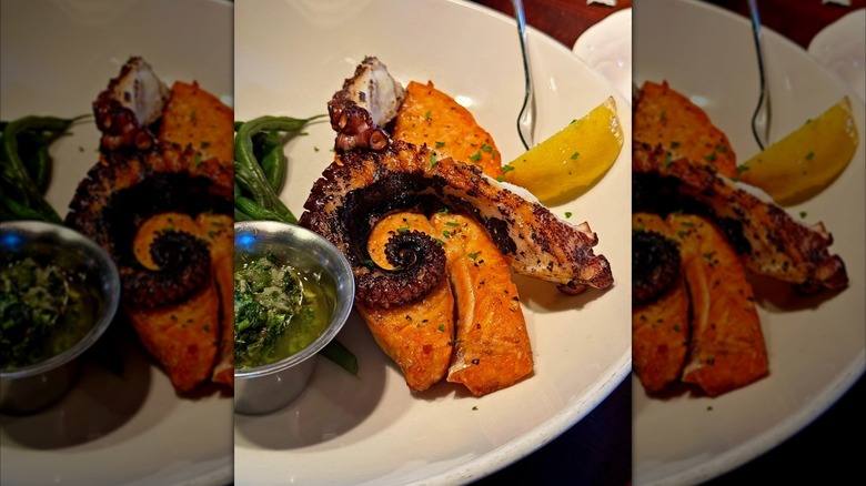 Plate of grilled ocotopus and salmon with green vegetables and lemon wedge