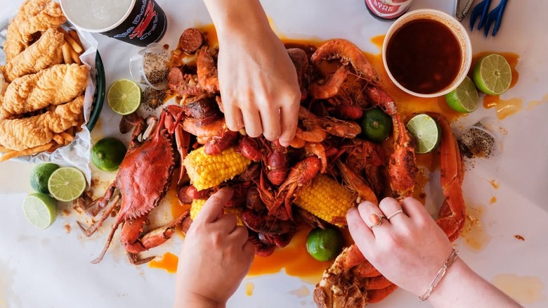 Top-down view of seafood boil spread, with hands picking up pieces