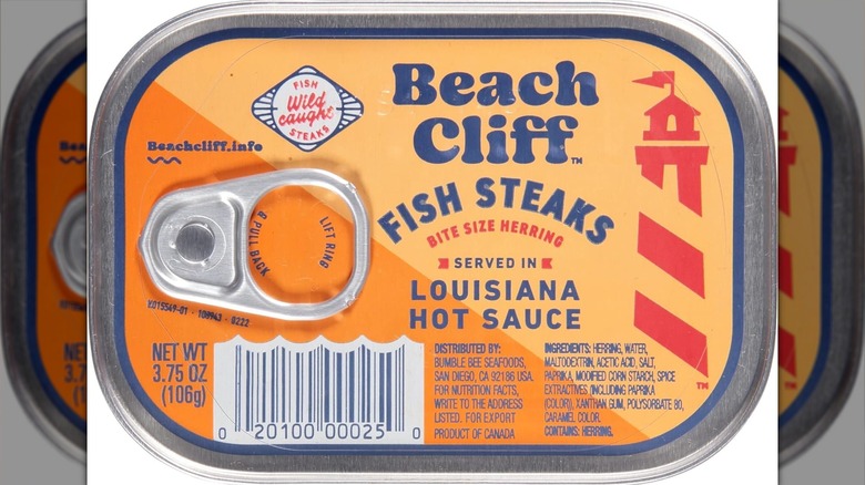 mirrored image of a closeup of a hand holding an open can of fish steaks