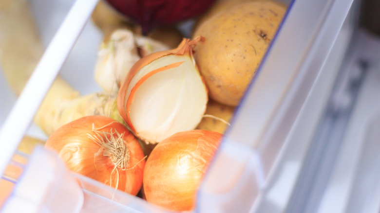 Halved and whole onions in fridge vegetable drawer with potatoes
