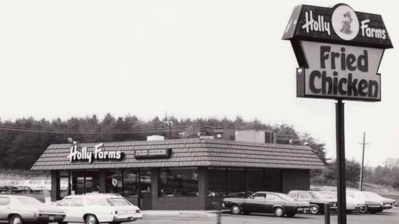 A Holly Farms storefront with a parking lot filled with cars, and a sign saying Holly Farms Fried Chicken on the side of the road