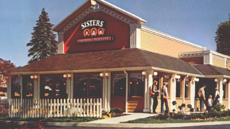 the storefront of a sisters chicken and biscuits outlet with white picket fence, yard, and home-style architecture