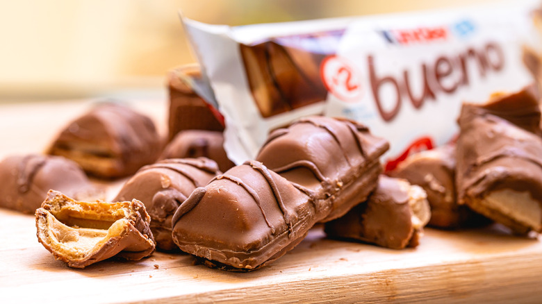 Close-up of Kinder Buenos unwrapped, whole and broken apart on a wood surface, with a wrapped package in the background