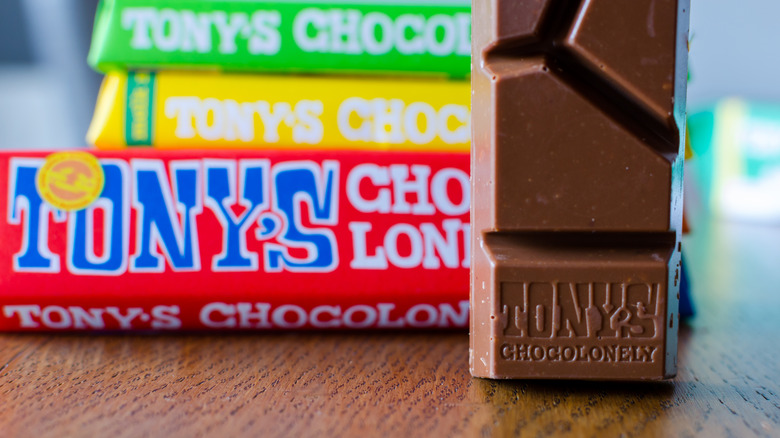 An unwrapped Tony's Chocolonely chocolate bar in the foreground with three wrapped bars in the background (with green, yellow, and red wrappers)