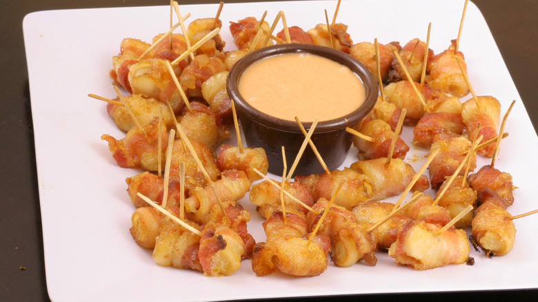 A plate of bacon-wrapped water chestnuts surrounding a dip cup