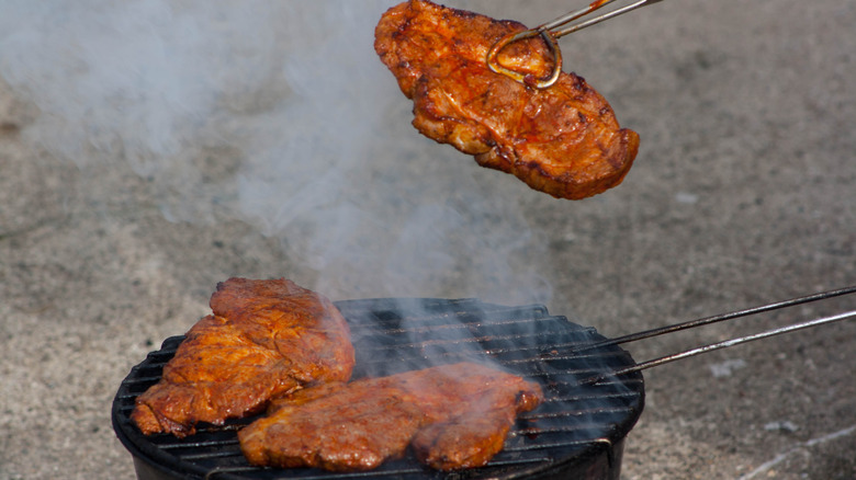 A steak being held by tongs above a grill with other steaks