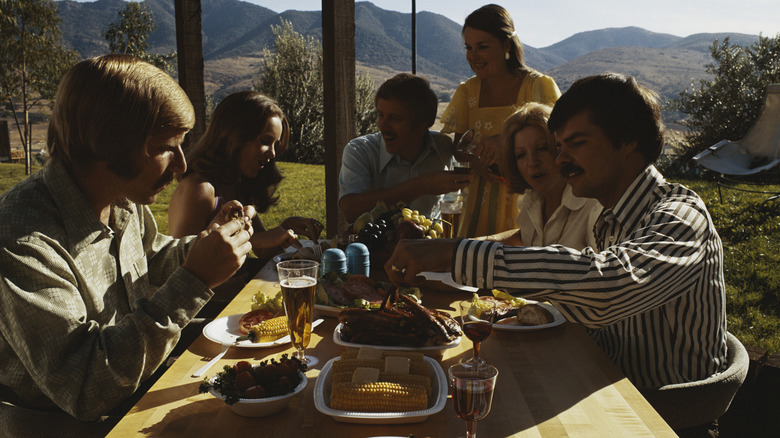 People sitting outdoors around a table full of food