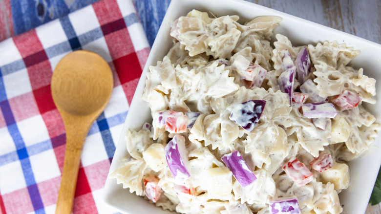 A plate of macaroni salad next to a wooden spoon on a plaid napkin