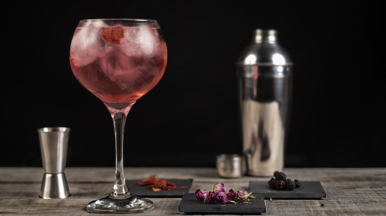 Pink cocktali with large ice cubes, shaker, and garnishes