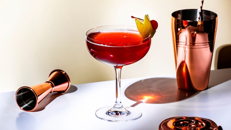 Red cocktail drink with whiskey, grenadine, bitter, lemon and ice with lemon zest and cherry. Beige background.