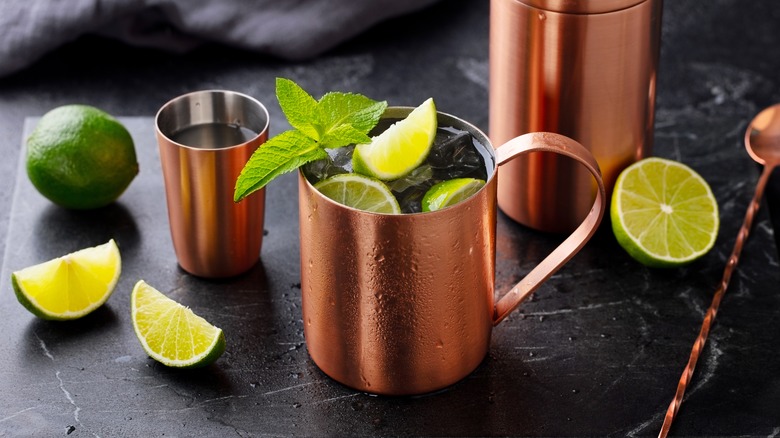 Moscow mule cocktail in copper mug, shaker with fresh mint, lime on marble board. Dark background. Close up.