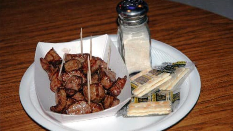 Small cubes of meat with toothpicks in a paper basket, saltines, and a salt shaker on a white plate