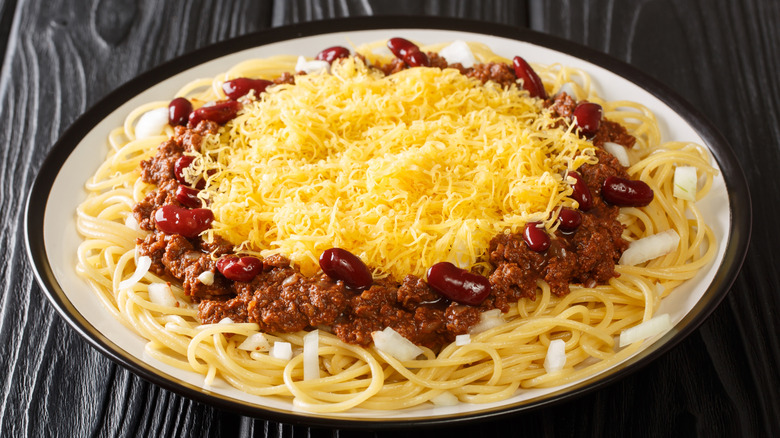 Spaghetti noodles, chili with beans, and lots of shredded cheese in a black and white bowl