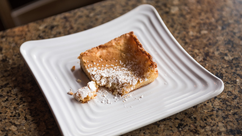 A square of gooey butter cake with a bite taken out of it on a white plate