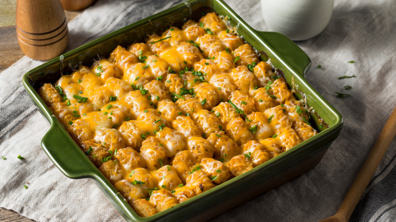 A tater tot casserole with cheese and herbs in a green casserole dish
