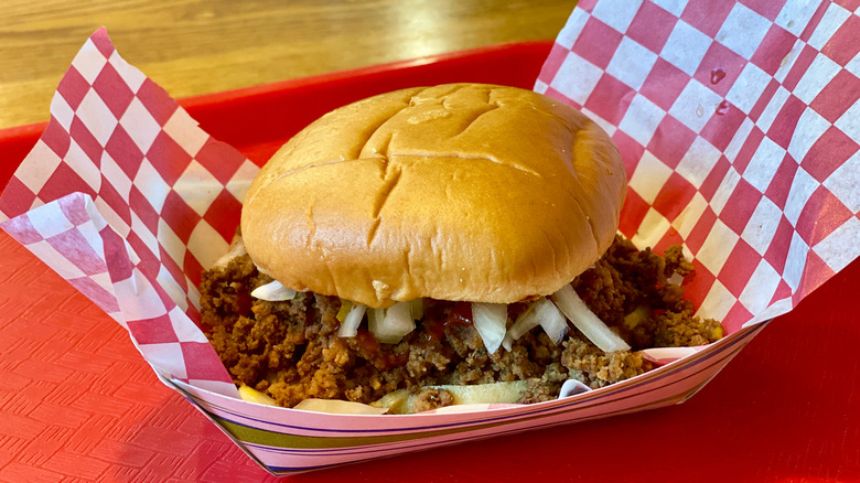 A loose meat sandwich from Maid-Rite in a basket with checkered paper on a red cafeteria-style tray
