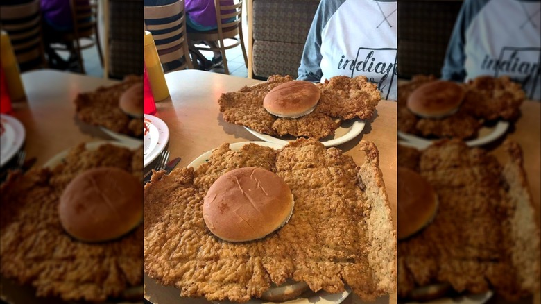 Two breaded pork tenderloin sandwiches with comically-large, flat meat on a diner table