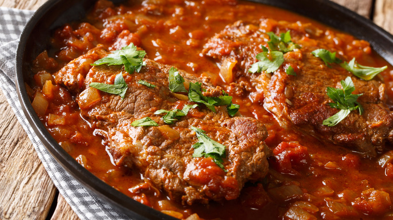A close up of a steak cooked in a sauce of peppers, tomatoes, and onions and garnished with herbs
