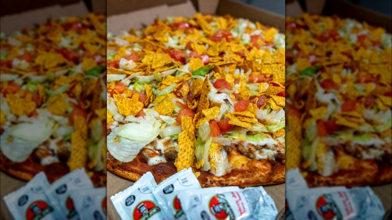 Happy Joe's taco pizza in a box next to white packets of taco sauce