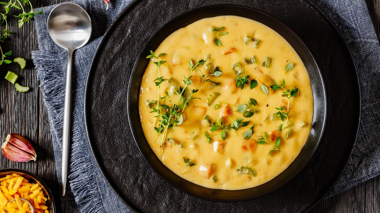 Beer cheese soup with vegetables and thyme in black bowl on dark wooden table.