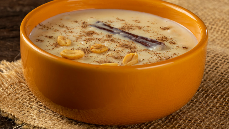 Corn hominy soup in an orange bowl on brown hessian mat.