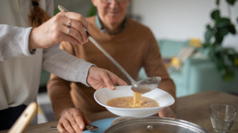 Woman serving up soup to man at dinner table.