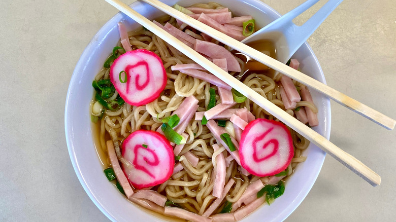 Saimin Hawaiian ramen noodles with Spam and Narutomaki fish roll, with chopsticks.