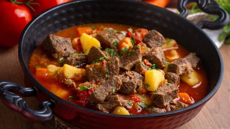 Black bowl of beef soup with vegetables.