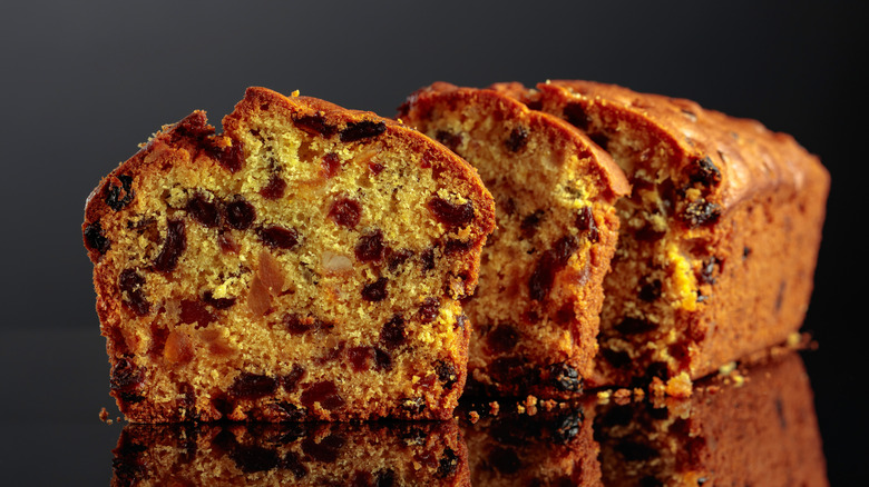 Cake with raisins and candied fruit on a black reflective background.