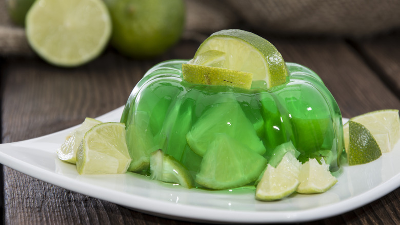 Lime Jell-O with sliced limes on a white plate on a wooden table