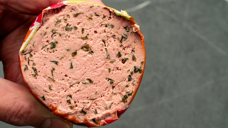 Hand holding cut liverwurst with herbs
