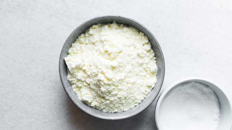 Overhead view of powdered milk in a grey bowl next to sugar bowl