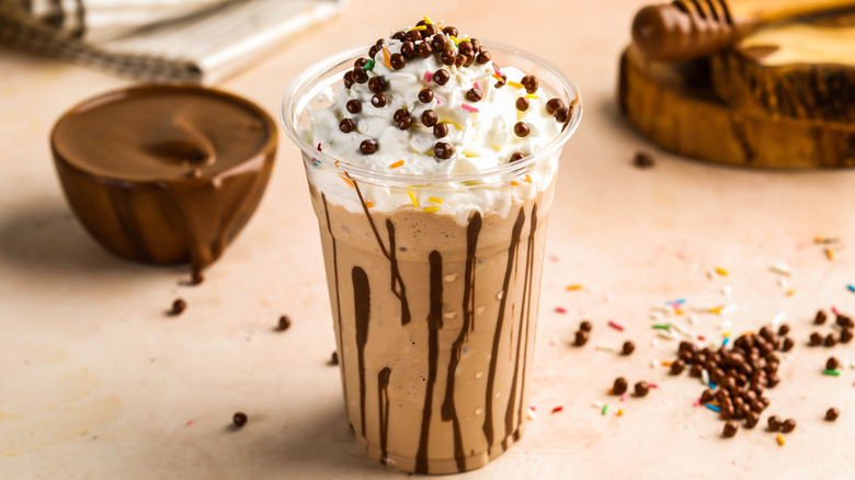 Chocolate milkshake in a plastic cup topped with whipped cream and sprinkles