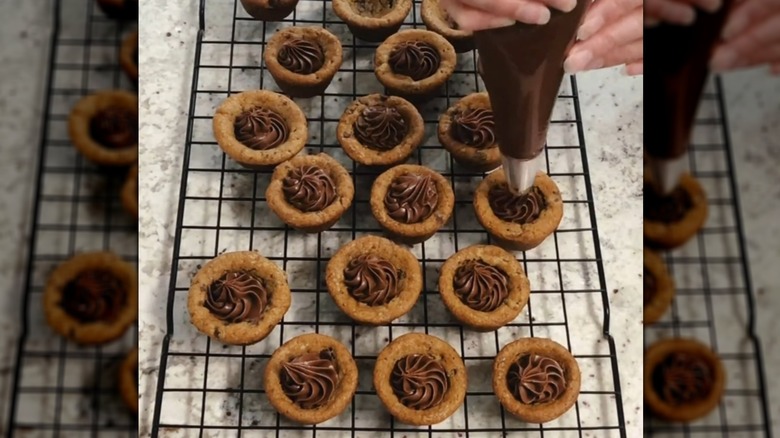 Piping chocolate filling into cookie cups on cooling rack