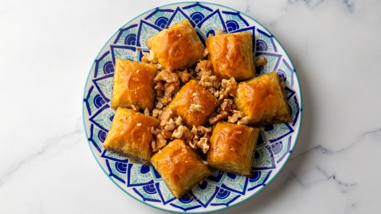 Baklava squares on blue patterned plate with chopped walnuts