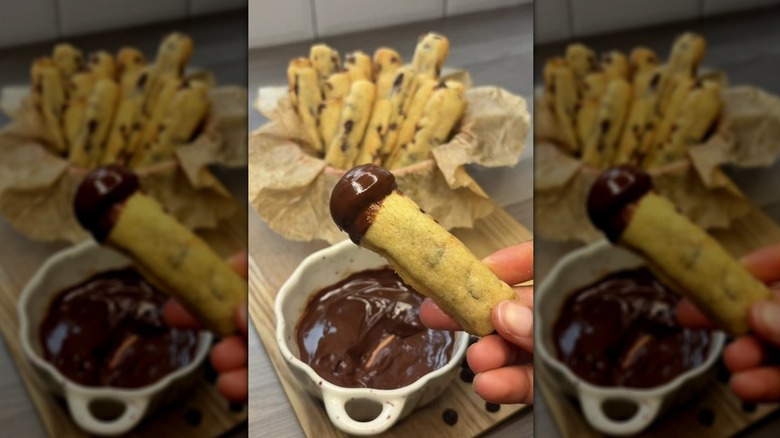 Hand holding chocolate chip cookie fry that's been dipped in chocolate sauce