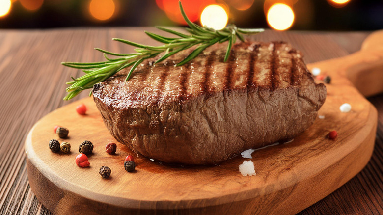 Steak on wooden cutting board with rosemary garnish